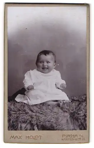 Fotografie Max Holdt, Pirna a / E., Portrait niedliches Kleinkind im weissen Kleid auf Fell sitzend