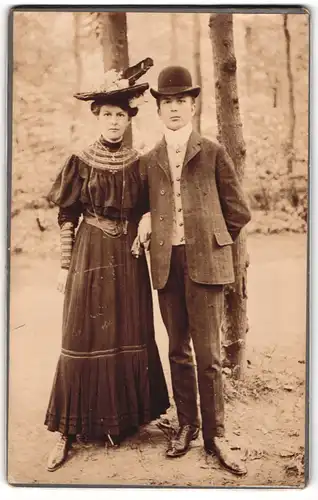 Fotografie unbekannter Fotograf und Ort, junges Paar im Anzug und im Kleid mit Federhut, Melone