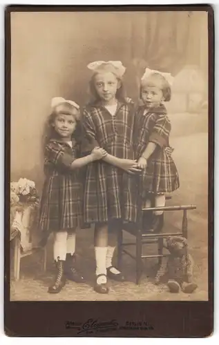 Fotografie Atelier Elegantz, Berlin, drei junge Mädchen in karierten Kleidern mit Teddy am Boden