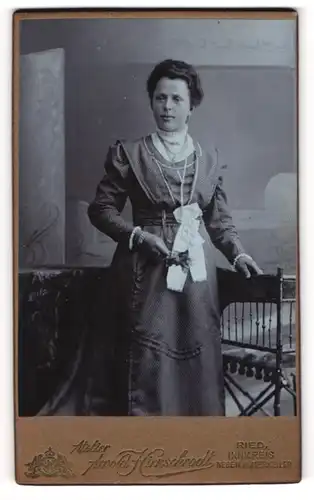 Fotografie Arnold Hirnschrodt, Ried, Dame in tailliertem Kleid mit weisser Schleife und Silberschmuck