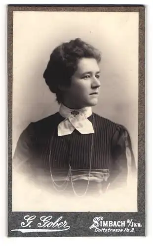 Fotografie G. Gober, Simbach a. Inn, Dultstr. 2, Junge Dame in dunklem Kleid mit weissem Halstuch und Brosche