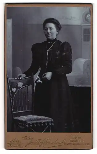 Fotografie Arnold Hirnschrodt, Ried, Junge Dame in dunklem Kleid mit Silberkette und Brosche hält Rosenstrauss