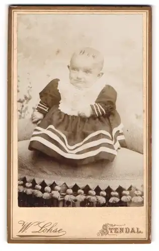 Fotografie W. Lohse, Stendal, Portrait sitzendes Baby im hübschen Kleid mit Latz