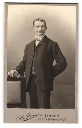 Fotografie Otto Haase, Hamburg, Portrait junger Herr im Anzug mit Fliege an Stuhl gelehnt