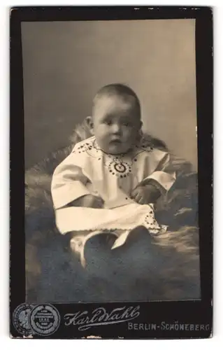 Fotografie Karl Wahl, Berlin-Schöneberg, Portrait niedliches Baby in hübscher Kleidung auf Fell sitzend