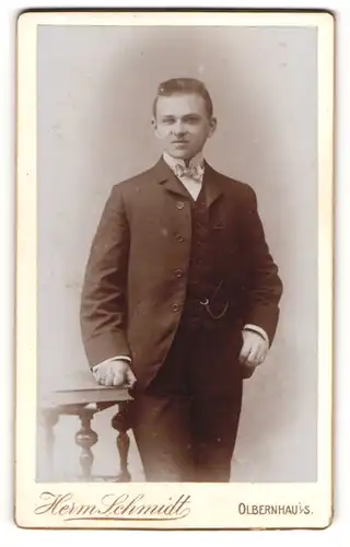 Fotografie Herm. Schmidt, Olbernhau i / S., Portrait elegant gekleideter Herr mit Buch an Tisch gelehnt