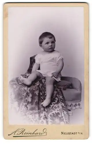 Fotografie A. Reinhard, Neustadt a / H., Portrait niedliches Kleinkind im weissen Hemd auf Decke sitzend