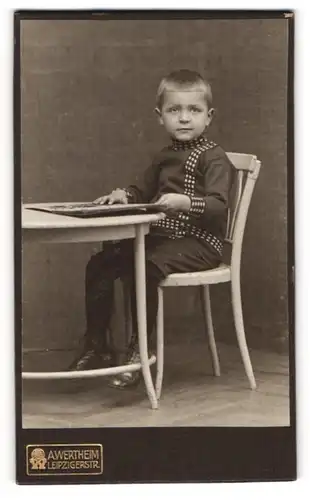 Fotografie A. Wertheim, Berlin, Portrait modisch gekleideter Junge mit Buch am Tisch sitzend