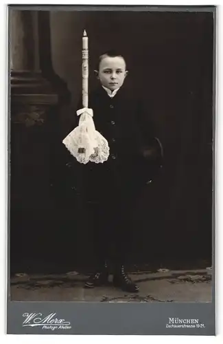 Fotografie W. Merx, München, junger Knabe im Anzug mit Kerze und Hut, Kommunion