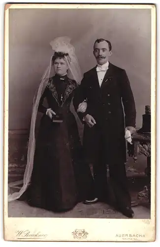 Fotografie W. Bruckner, Auerbach i. V., Eheleute im schwarzen Brautkleid und Anzug mit Fliege