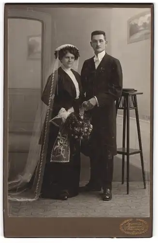 Fotografie Hermann Luh, Seifhennersdorf i. S., Brautpaar im schwarzen Hochzeitskleid und Anzug mit Brautstrauss