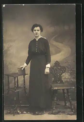 Foto-AK Junge Dame im schwarzen Kleid mit Buch in der Hand vor Studiokulisse