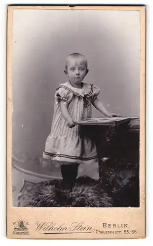 Fotografie Wilhelm Stein, Berlin, kleines Kind im hellen Kleid blättert in eimem Album