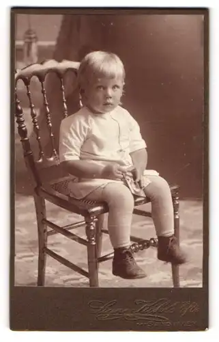 Fotografie Signe Kihls Eftr., Sandviken, Portrait sitzendes Kind in hübscher Kleidung mit Fotos