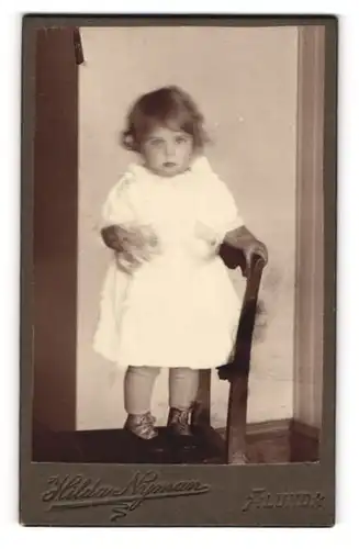 Fotografie Hilda Nyman, Alunda, Portrait kleines Mädchen im weissen Kleid auf Stuhl stehend