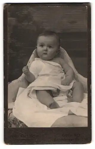 Fotografie Curt Meyer, Berlin-NO, Portrait sitzendes Baby im weissen Hemd mit nackigen Füssen