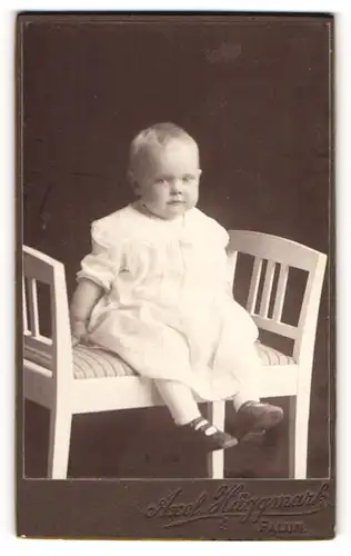Fotografie Axel Häggmark, Falun, Portrait niedliches Kleinkind im weissen Kleid auf Bank sitzend