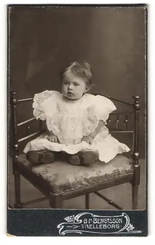 Fotografie B. P. Bengtsson, Trelleborg, Kleinkind in weissem Spitzenkleid auf Stuhl sitzend