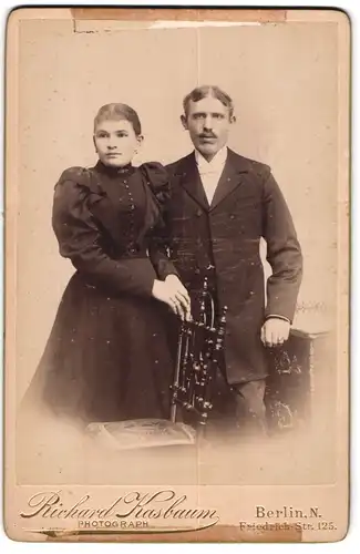 Fotografie Richard Kasbaum, Berlin-N, Portrait modisch gekleidetes Paar an Stuhl gelehnt