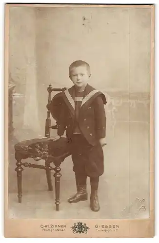 Fotografie Chr. Zimmer, Giessen, Portrait kleiner Junge im Matrosenanzug an Stuhl gelehnt
