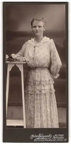 Fotografie Alfred Petersen, Berlin, Portrait junge Dame im modischen Kleid an Tisch gelehnt