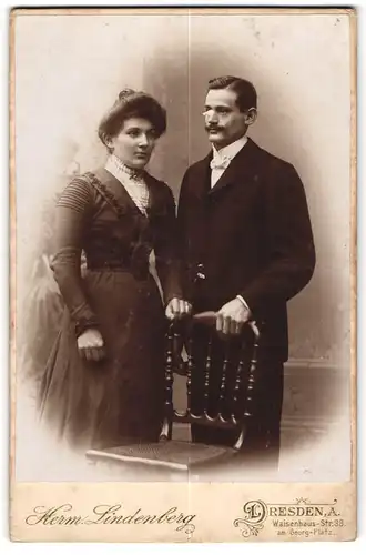 Fotografie Herm. Lindenberg, Dresden-A, Portrait elegant gekleidetes Paar an Stuhl gelehnt