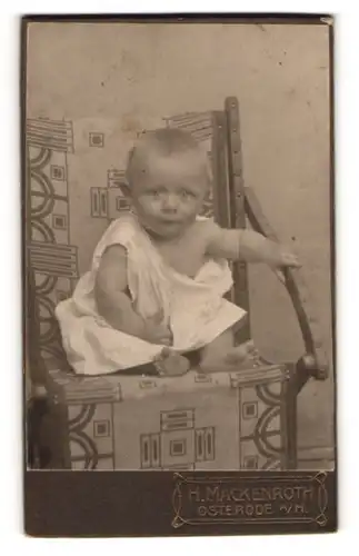Fotografie H. Mackenroth, Osterode a. H., Baby halb angezogen im Stuhl