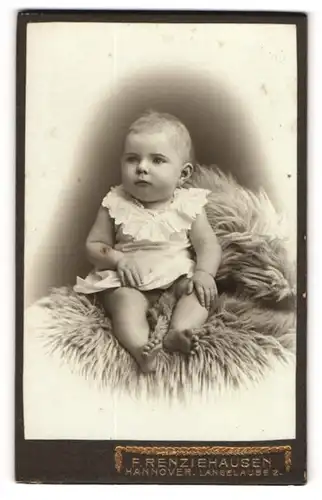 Fotografie F. Renziehausen, Hannover, Kleinkind im Hemd auf Tierfell sitzend