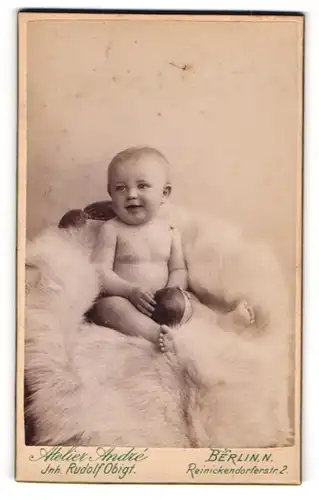 Fotografie Atelier André, Berlin, lachendes nacktes Kleinkind mit ball auf Fell sitzend