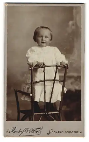 Fotografie Rudolf Flohr, Neckarbischofsheim, Portrait lächelndes Mädchen im weissen Kleidchen auf einem Stuhl stehend