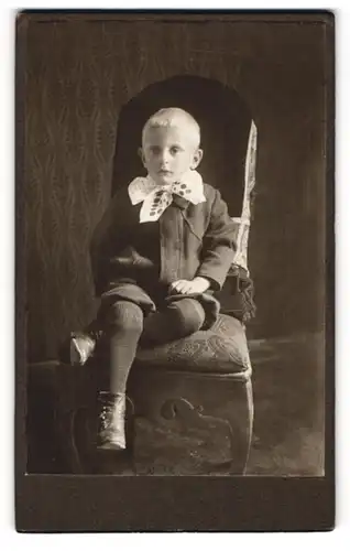 Fotografie unbekannter Fotograf und Ort, Portrait Bub in festlicher Kleidung auf Sitzmöbel