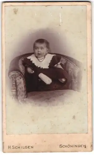 Fotografie H. Schilgen, Schöningen, Portrait niedliches Kleinkind im hübschen Kleid auf Sessel sitzend