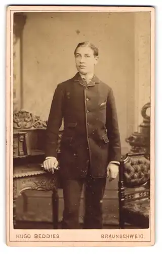 Fotografie Hugo Beddies, Braunschweig, Portrait modisch gekleideter Mann an Schreibtisch gelehnt