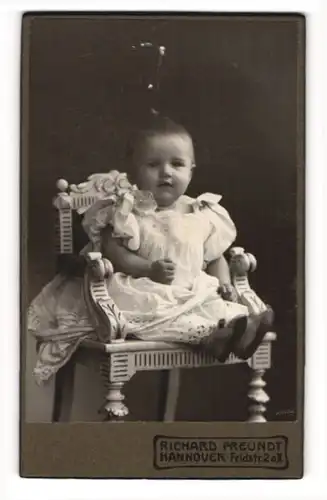 Fotografie Richard Freundt, Hannover, Portrait niedliches Kleinkind im hübschen Kleid sitzt auf Stuhl