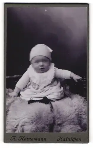 Fotografie A. Heinemann, Hainichen, Portrait niedliches Baby im weissen Kleid auf Fell sitzend