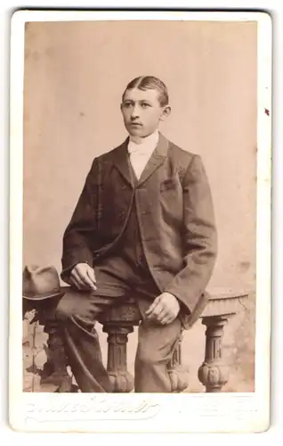 Fotografie Max Rother, Rosswein, Portrait modisch gekleideter Mann mit Hut auf Geländer sitzend