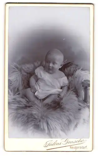 Fotografie Julius Grusche, Neugersdorf, Portrait niedliches Kleinkind im weissen Hemd auf Fell sitzend