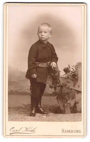 Fotografie Carl Koch, Hamburg, Portrait modisch gekleideter Junge an Zaun gelehnt