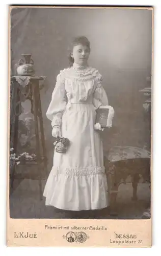 Fotografie L. K. Jué, Dessau, Portrait junge Dame im weissen Kleid mit Buch und Blumen