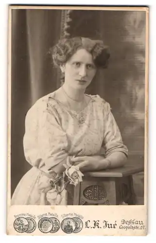 Fotografie L. K. Jué, Dessau, Portrait bürgerliche Dame mit Blume an Tisch gelehnt