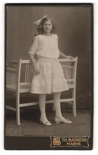 Fotografie Th. H. Backens, Marne, Portrait junge Dame im weissen Kleid an Bank gelehnt