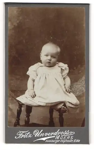Fotografie Fritz Unverdross, Moers, Portrait niedliches Kleinkind im hübschen Kleid mit nackigen Füssen