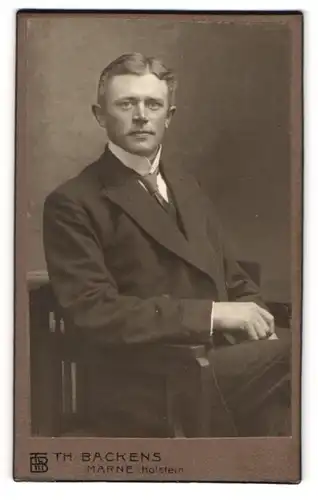 Fotografie Th. Backens, Marne i. Holstein, Portrait junger Herr im Anzug mit Krawatte auf Stuhl sitzend