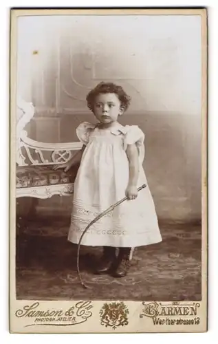 Fotografie Samson & Co., Barmen, Portrait kleines Mädchen im weissen Kleid mit Peitsche