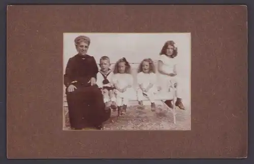 Fotografie Fotograf und Ort unbekannt, Grossmutter & Enkelkinder auf Bank sitzend
