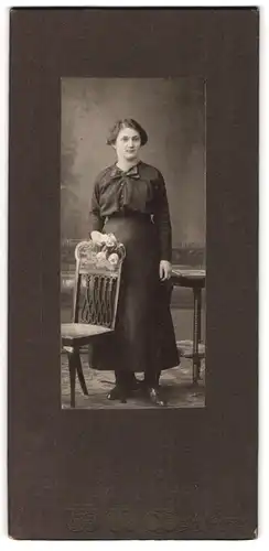 Fotografie L. K. Jue, Dessau, Frau im schwarzen Kleid stehend an einem Stuhl