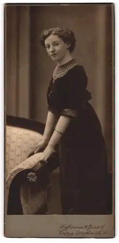 Fotografie Hoffmann & Jursch, Leipzig, Junge Dame im schwarzen Kleid stehend an einem Sofa