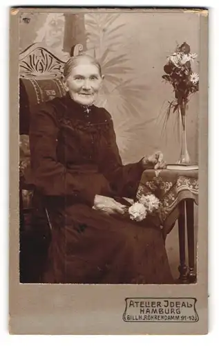 Fotografie Atelier Ideal, Hamburg, Ältere Dame im schwarzen Kleid mit Blumen sitzend