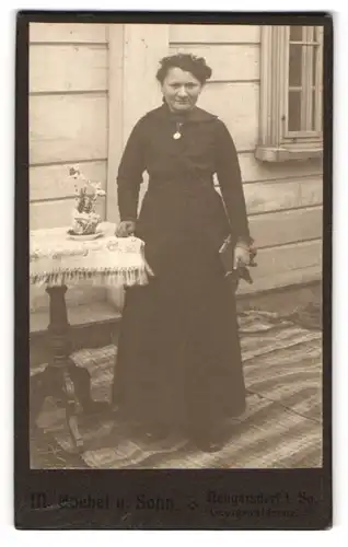 Fotografie M. Goebel & Sohn, Neugersdorf i. Sa., Frau im schwarzen Kleid stehend an einem Tisch