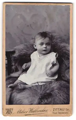 Fotografie Atelier Walbrecher, Zittau, Baby in weissem Laibchen sitzt auf einer Felldecke